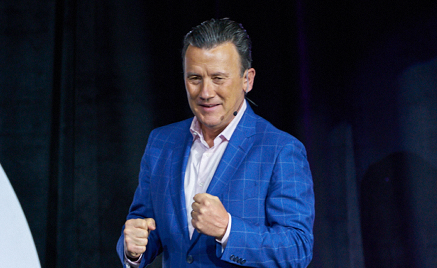 Man in blue suit speaking on stage with a headset microphone