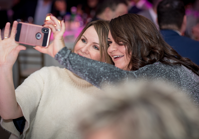 Two women smiling while taking a selfie together at an event.